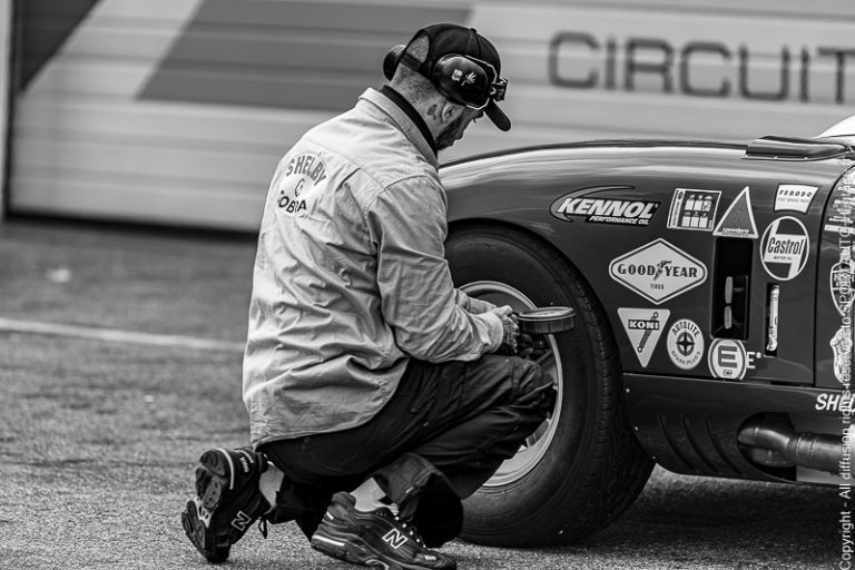 Un mécanicien en train de mesurer la pression des pneus d'une voiture de course sur un circuit.