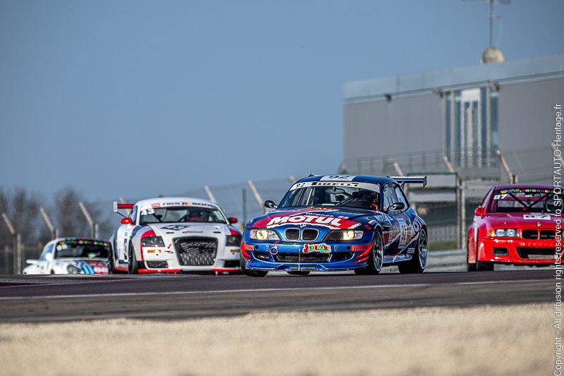 Voiture de course BMW bleue avec sponsor sur un circuit, entourée d'autres voitures de course.