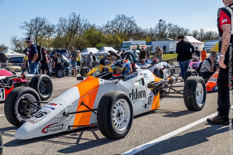 Voiture de course monoplace blanche et orange avec le numéro 16 sur la grille de départ.