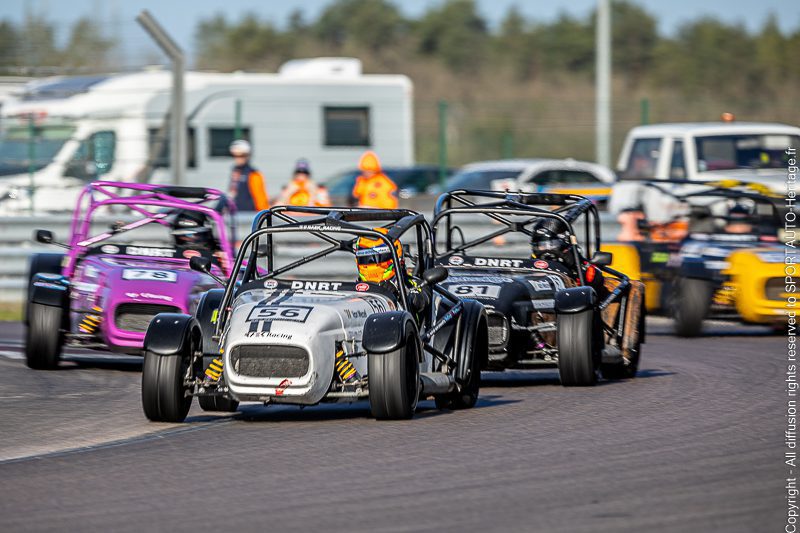 Trois voitures de course sur un circuit, deux en premier plan et une en arrière-plan, avec des pilotes à l'intérieur.