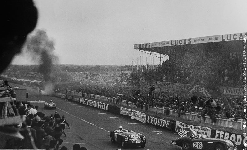La Mercedes 300 SLR de Pierre Levegh brûle en arrière-plan, tandis que l'Austin Healey n° 26 de Lance Macklin gît sur la piste, à l'endroit même où elle s'est immobilisée après l'accident. La MG n° 64 de Ted Lund et Hans Waeffler passe devant l'épave et termine sa course à la 17e place.